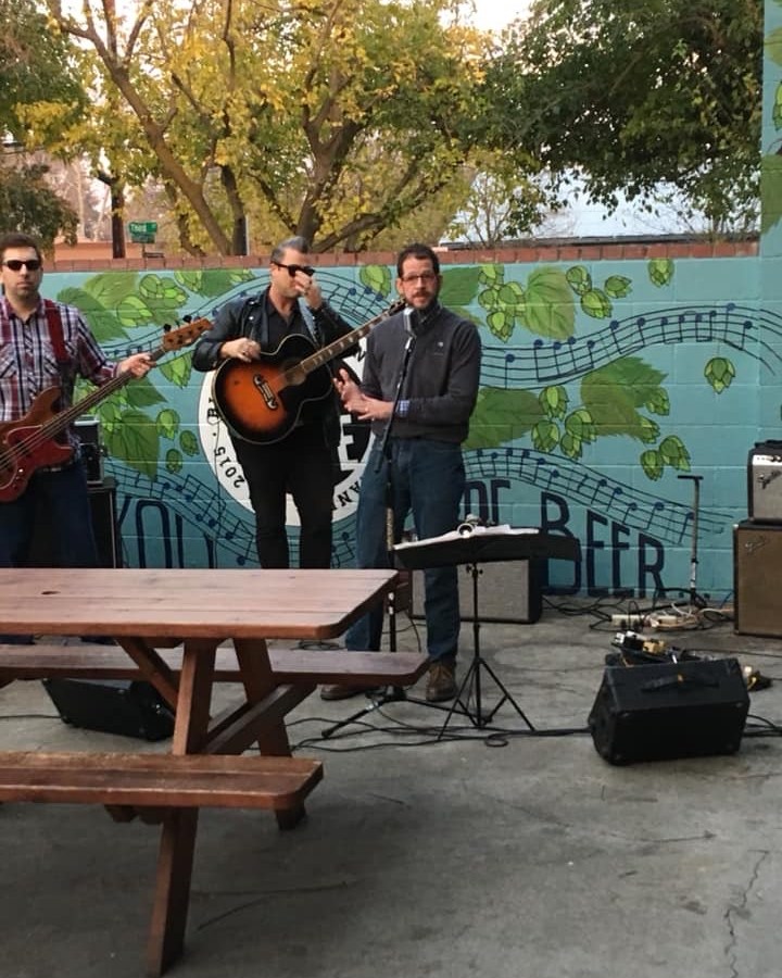 Musicians and a speaker performing outdoors beside a mural at Berryessa Brewing