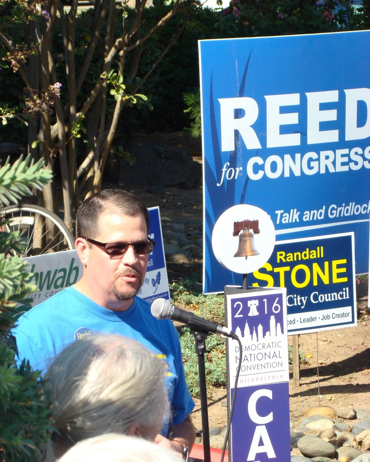 Candidate speaking into a microphone beside 2016 campaign and Democratic National Convention signs