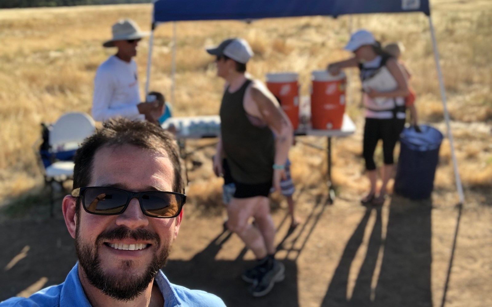 Volunteer taking a selfie beside a shaded hydration station in open country