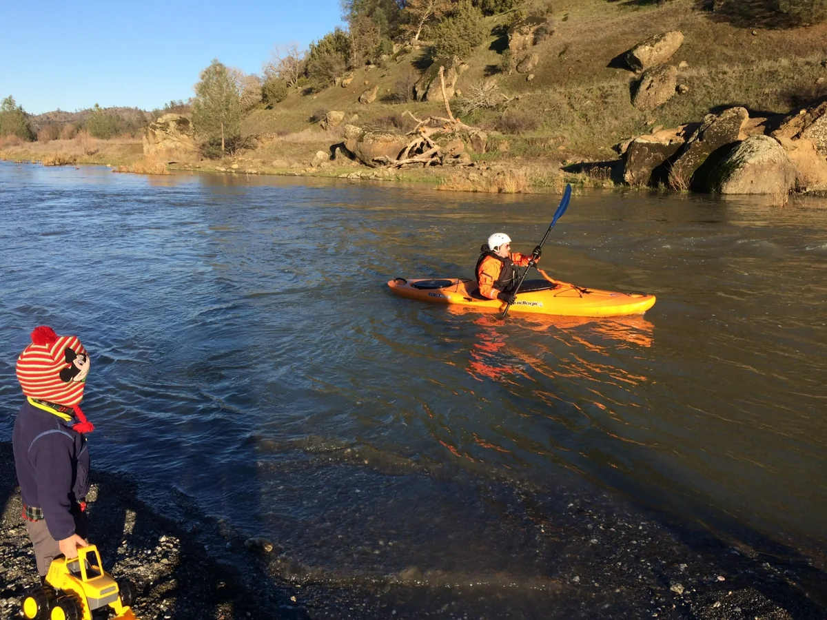 Randall Stone kayaking while young Rhys watches from the riverbank