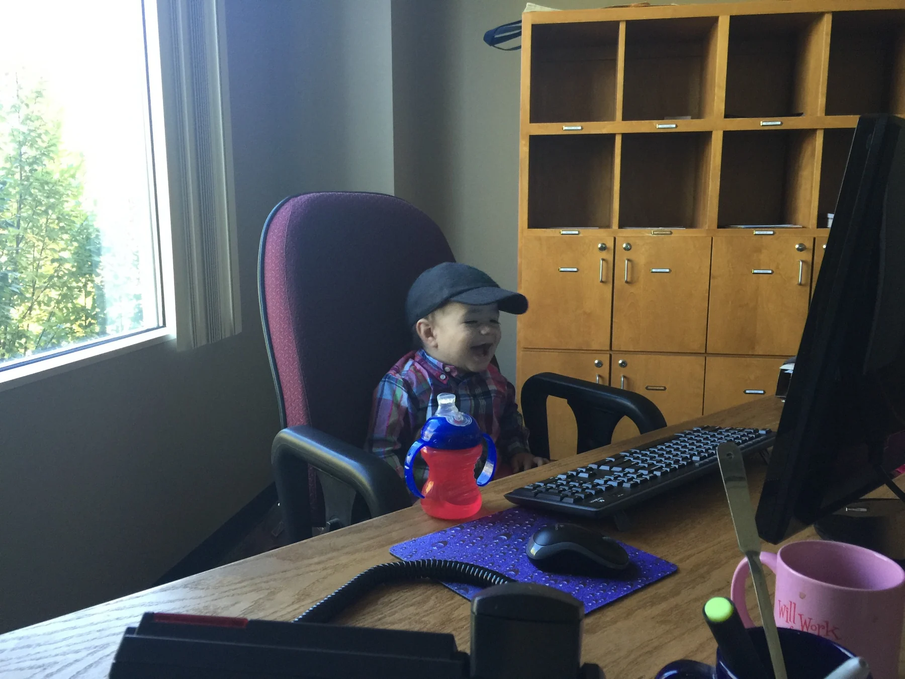 Toddler Rhys Stone sitting in Randall Stone’s office chair beside a keyboard and computer