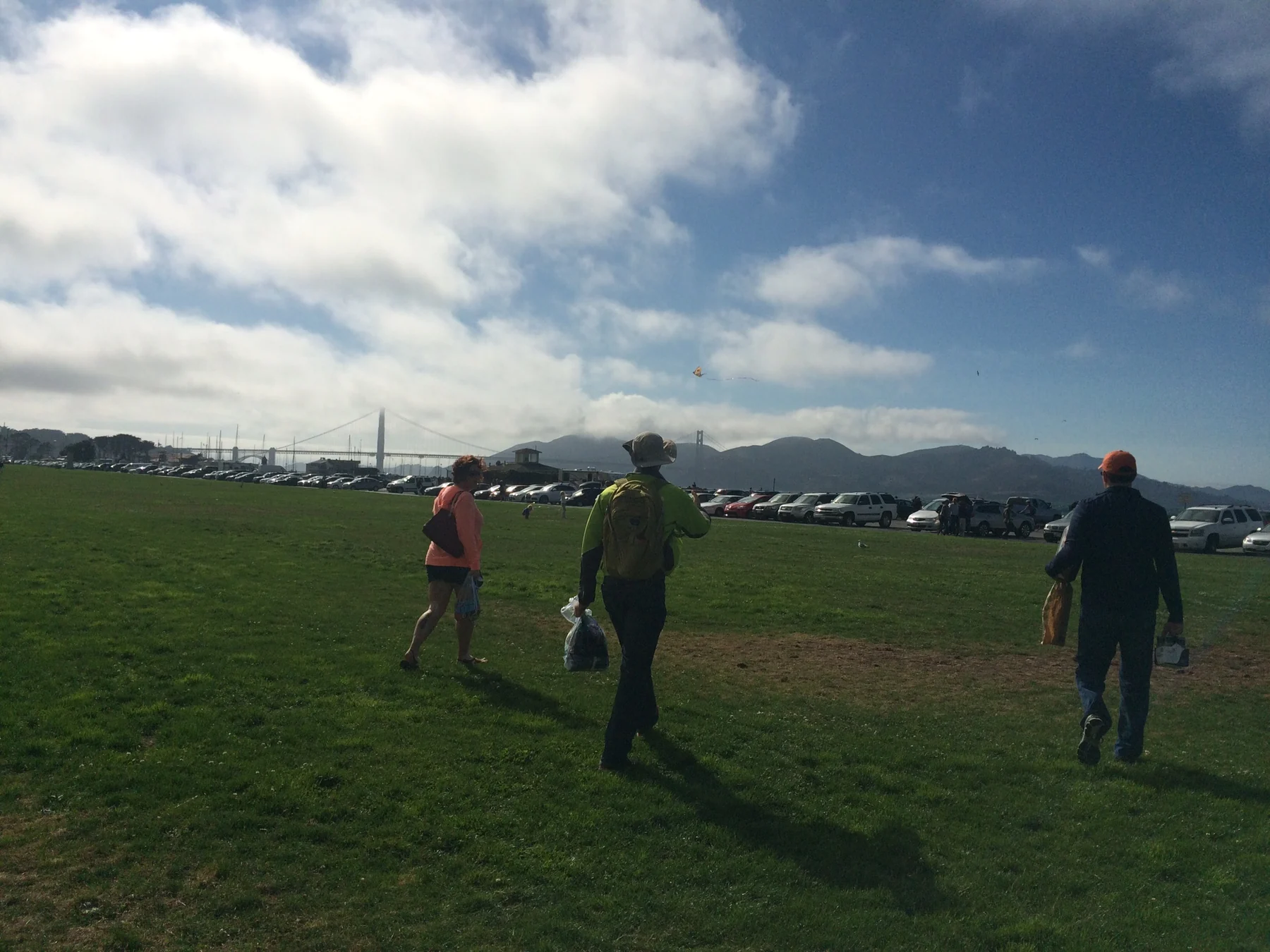 People walking across a grassy San Francisco waterfront area with the Golden Gate Bridge in the background