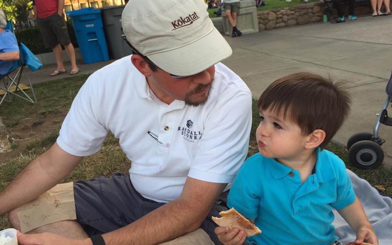 Adult and child sharing food while seated at an outdoor community gathering