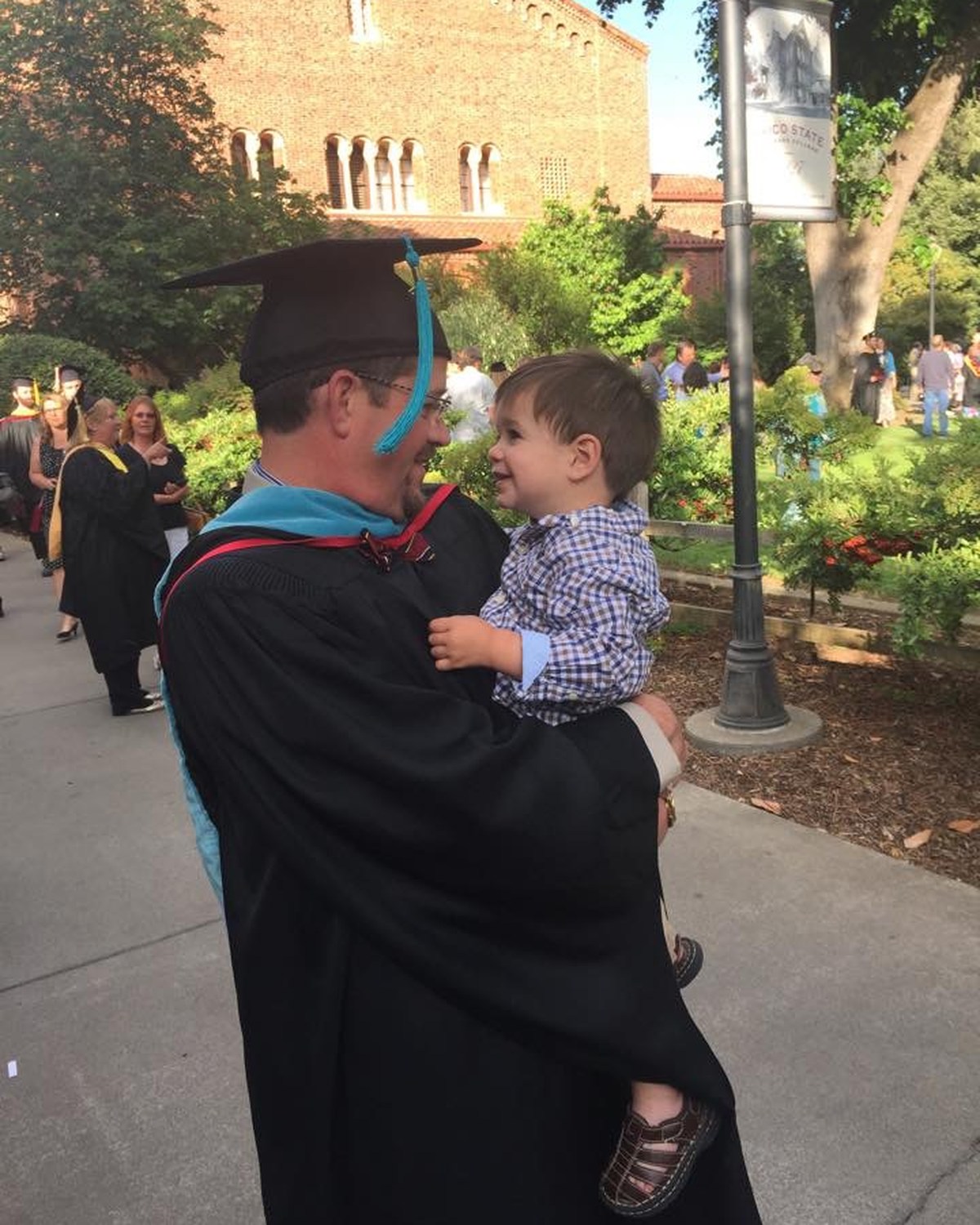 Graduate in academic regalia holding a young child after commencement