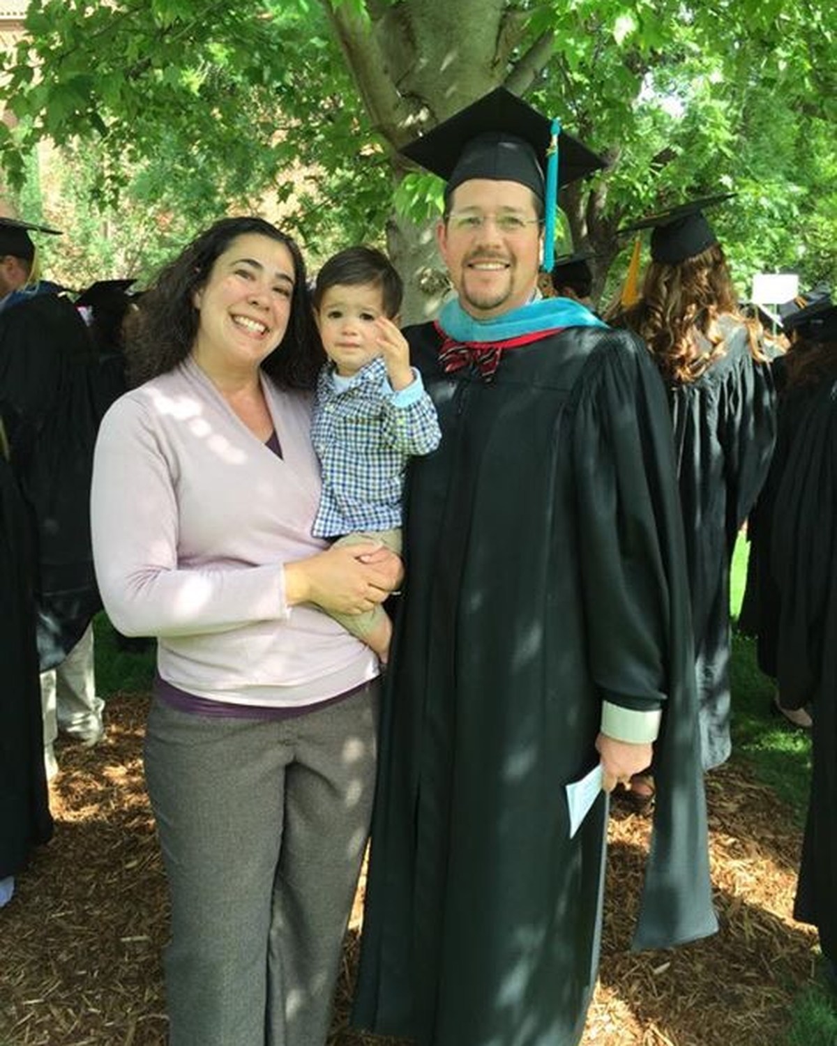 Graduate in academic regalia standing with family at an outdoor commencement