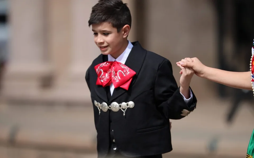 A young charro performer holding a dancer’s hand during a Rosas de María performance