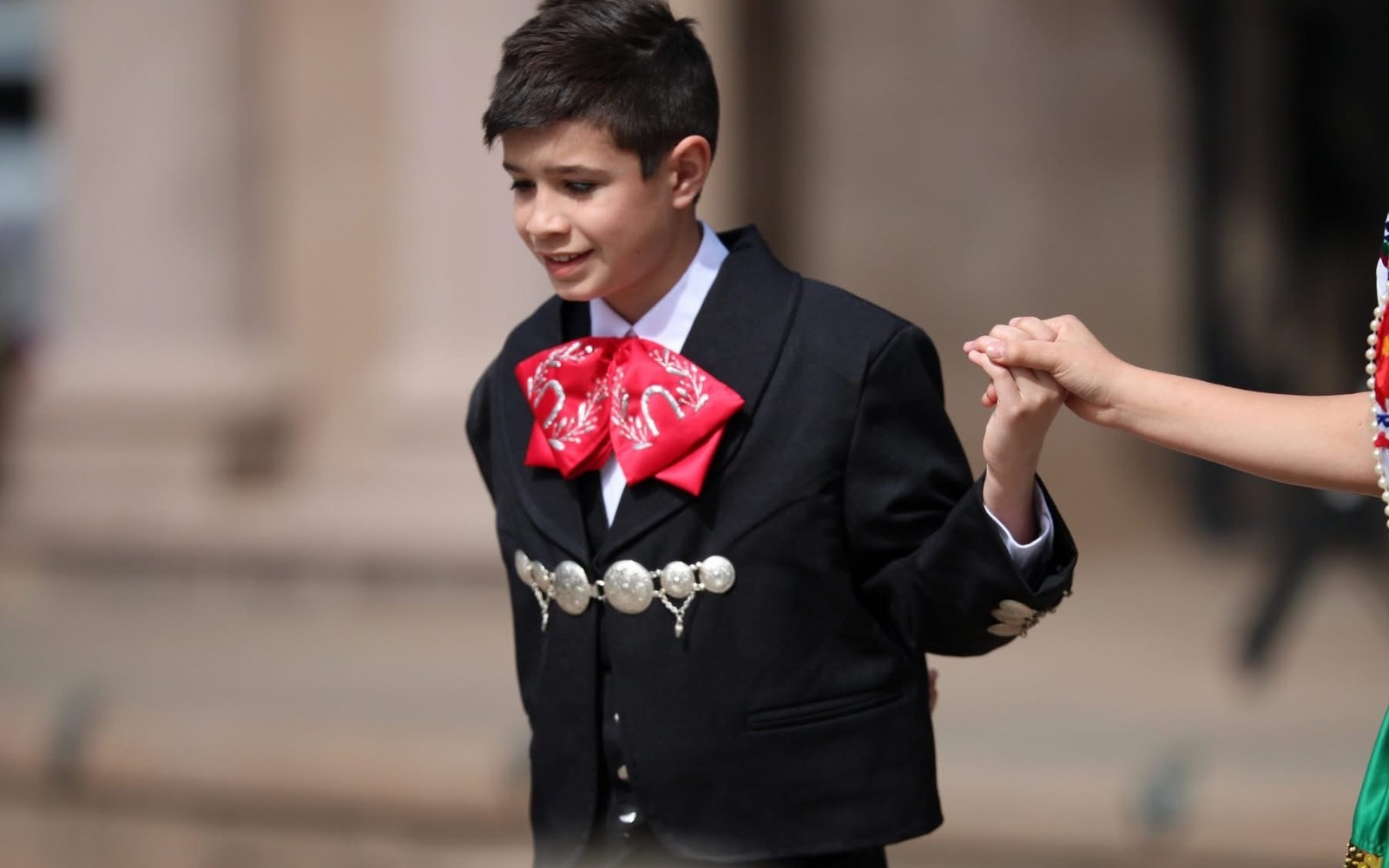 Young charro performer joining hands with another dancer during a Ballet Folklórico performance