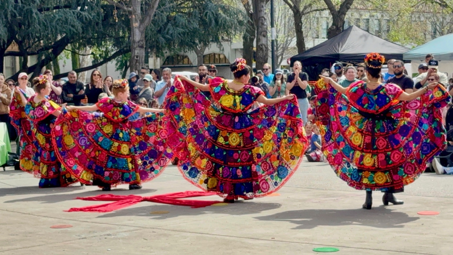 Rosas de María dancers performing in embroidered floral dresses before an outdoor audience