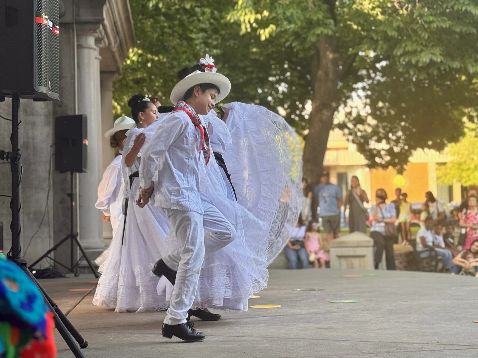 Ballet Folklórico Rosas de María dancers in white performing outdoors at Chico City Hall, with a young charro performer in profile in the foreground